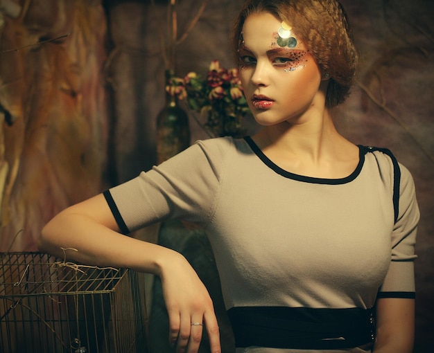 Fashion model woman with creative make up sitting on a stool in drama decoration