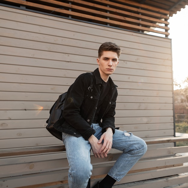 Fashion model young stylish man in fashionable jeans clothes sits