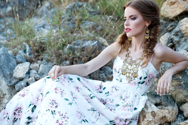 Fashion outdoor photo of beautiful woman with dark braids hair in luxurious white dress posing in summer field. Bride. Beautiful boho girl looking away.