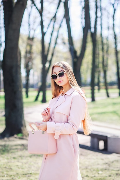 Fashion outdoor photo of beautiful young woman with blond hair in elegant clothes and sunglasses posing in sunny park