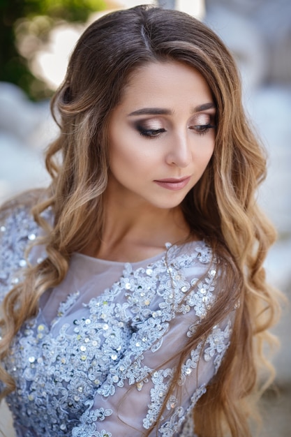 Fashion outdoor photo of elegant beautiful woman with blond hair in luxurious sequins dress and silver accessories,posing in summer park