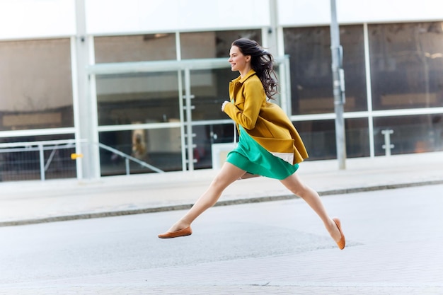 fashion and people concept - happy young woman or teenage girl running and jumping high on city street