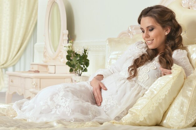 Fashion photo of beautiful pregnant woman with long dark hair posing in cozy interior