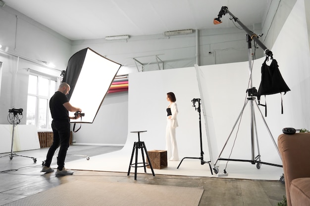 Fashion photography in a photo studio. Professional male photographer taking pictures of beautiful woman model on camera, backstage