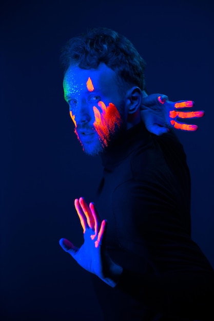 Фото Модный портрет мужчина с флуоресцентной краской на лице под неоновым светом