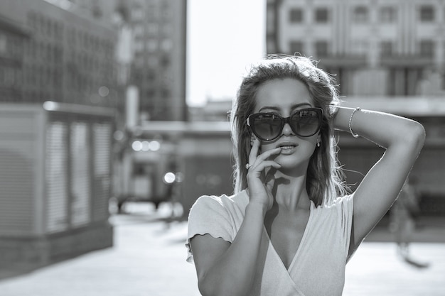 Fashion portrait of adorable young model in glasses walking down the street. Empty space. Monochrome color