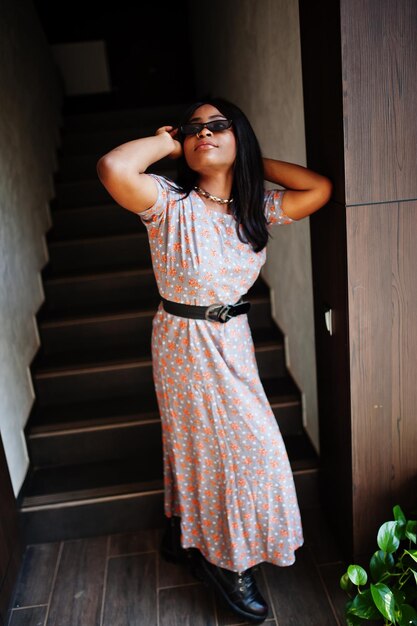 Fashion portrait of african american woman in long dress boots and sunglasses indoor