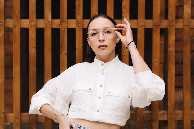 Fashion portrait of an attractive brunette with straight hair. woman dressed in a white blouse and glasses posing