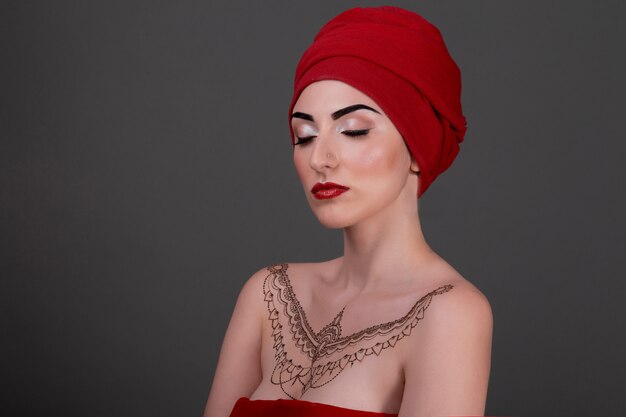 Модный портрет красивой чувственной женщины, закрытого очима, красной шали, вечернего макияжа и татуировки хной на коже