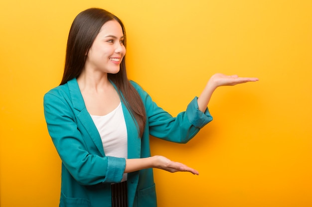 Fashion portrait of beautiful woman in green suit  showing something ON HER hand  on yellow background