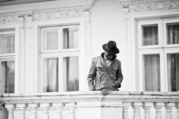 Adatti il ritratto dell'uomo afroamericano nero sul mantello del cappotto verde e sul cappello nero, rimanga sul balcone del palazzo giallo. foto in bianco e nero