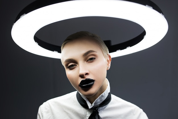 Fashion portrait of a blonde with lipstick black on the lips. Background is a lamp.