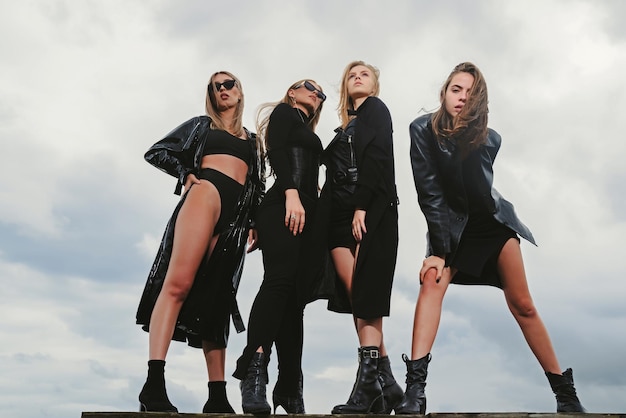 Fashion portrait of group fashion models girls posing outdoor black style outfit against sky attract