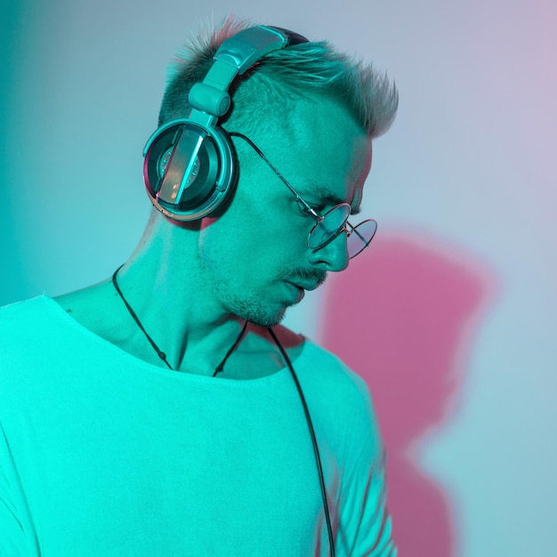 Photo fashion portrait of handsome young man listening to music with headphones in studio with creative light