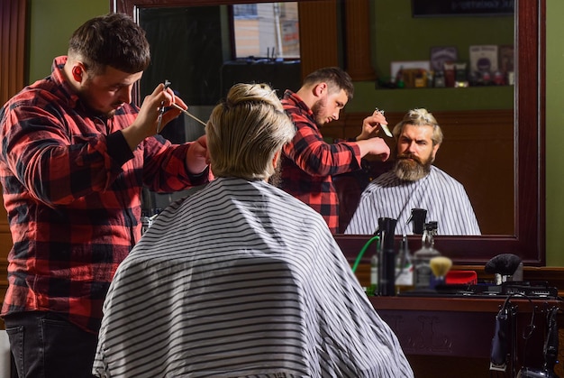 Fashion portrait of man Barbershop Young hipster man with beard cutting his hair in a barbershop Professional hairdressing work Lifestyle master barber does the hairstyle and styling with dryer