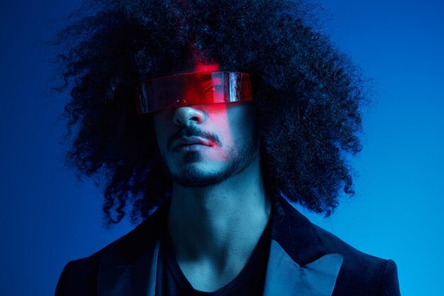 Fashion portrait of a man with curly hair on a blue background wearing red sunglasses multinational colored light trendy modern concept