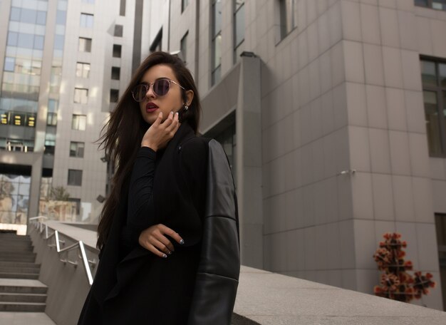 Fashion portrait of model in trendy coat and stylish glasses posing at the building