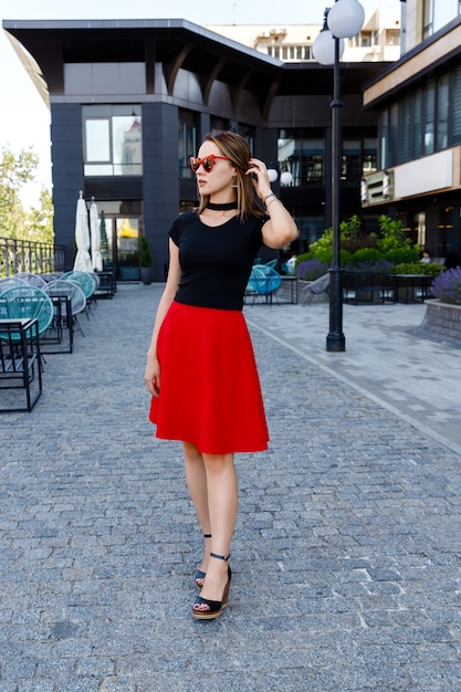 通りを歩いて黒のtシャツと赤いスカートのきれいな女性のファッションの肖像画。トレンディな服のメガネアクセサリー。ショッピング販売コンセプト