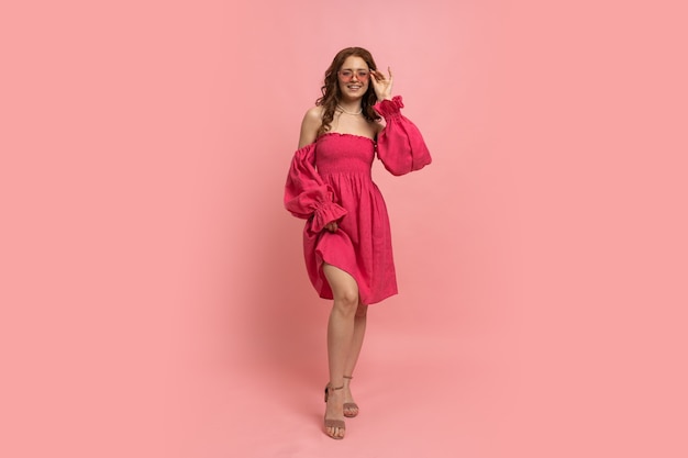 Fashion portrait of stylish red-haired woman posing on pink lien dress with sleeves on pink