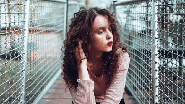 Fashion portrait of trendy young woman sitting near the netting rabitz in the city