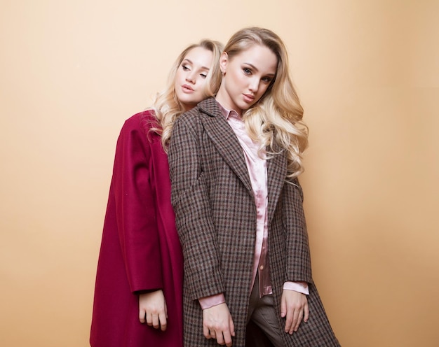 Fashion portrait of two girls best friends posing indoor on beige background wearing winter stylish coat