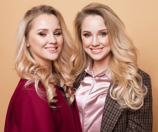 Fashion portrait of two girls best friends posing indoor on beige background wearing winter stylish coat