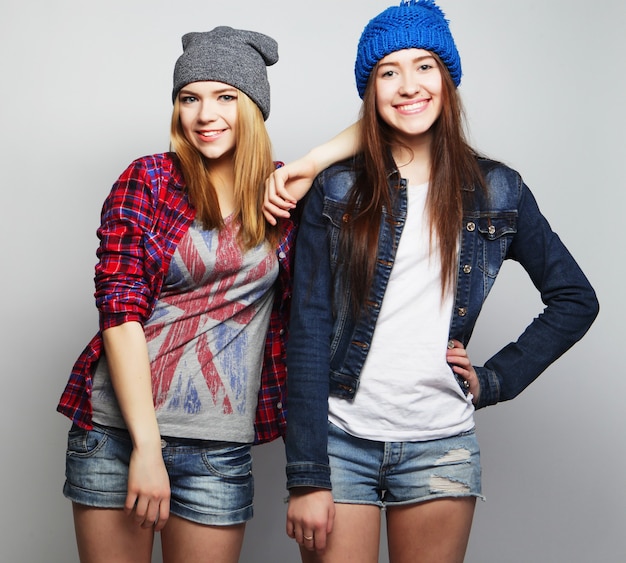 Fashion portrait of two stylish sexy hipster girls best friends, wearing cute swag outfits and hats.  