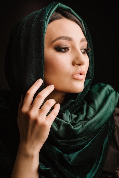Модный портрет женщины в зеленом шарфе или хиджабе, позирующей на темном фоне