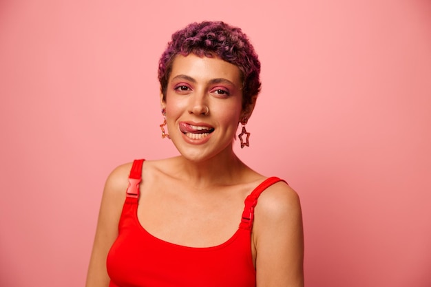 Photo fashion portrait of a woman with a short haircut of purple color and a smile with teeth in a red top on a pink background happiness high quality photo