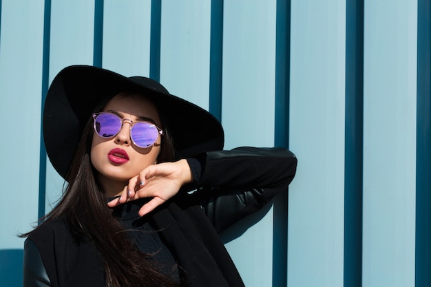 Fashion portrait of young beautiful model in stylish glasses wears black hat. Outdoor lifestyle portrait