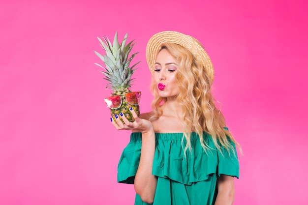 Foto giovane bella donna del ritratto di modo con l'ananas sopra la parete rosa