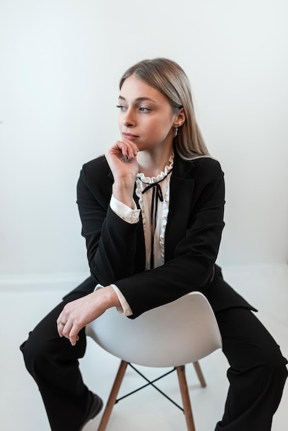 Fashion portrait of young blonde caucasian woman in trendy suit sitting on chair isolated on white Studio shoot