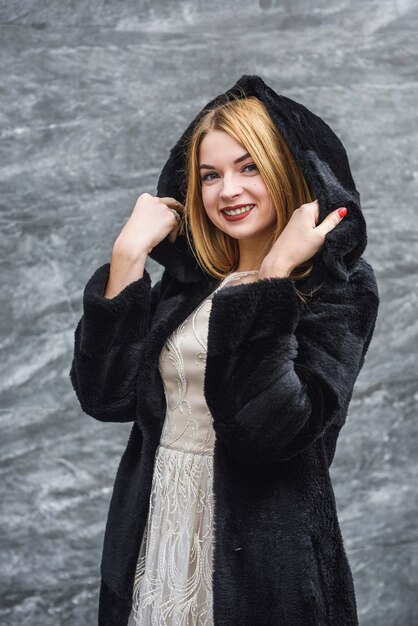 Fashion portrait of young blonde elegant woman in black dress and black fur coat at city street