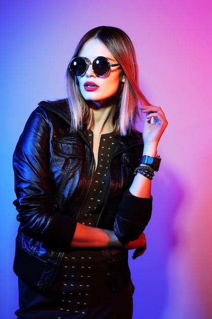 Fashion portrait of young elegant woman in sunglasses. Black leather jacket, colored background, studio shot