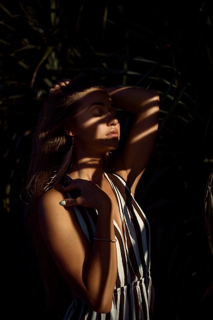 Fashion portrait of a young European girl in profile with a striped shadow from the green leaf. 