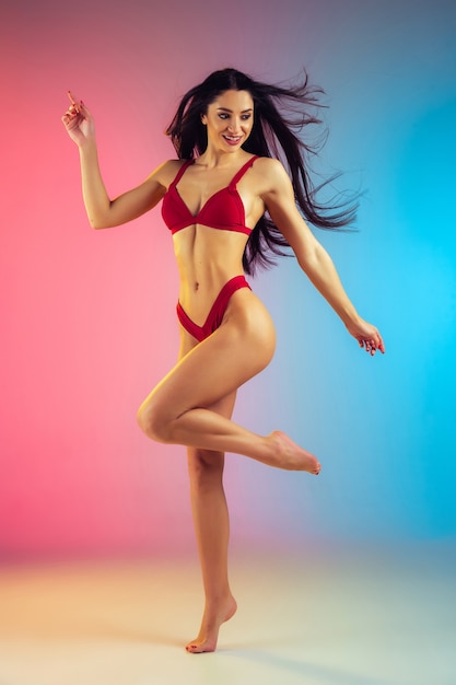 Fashion portrait of young fit and sportive woman in stylish red luxury swimwear on gradient wall perfect body ready for summertime