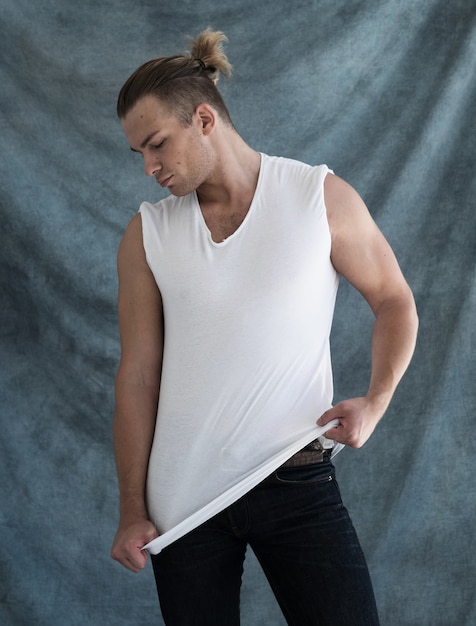 Fashion portrait of young man in white shirt poses in studio over blue background