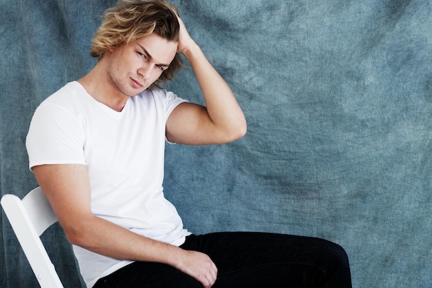 Fashion portrait of young man in white shirt poses in studio over blue background