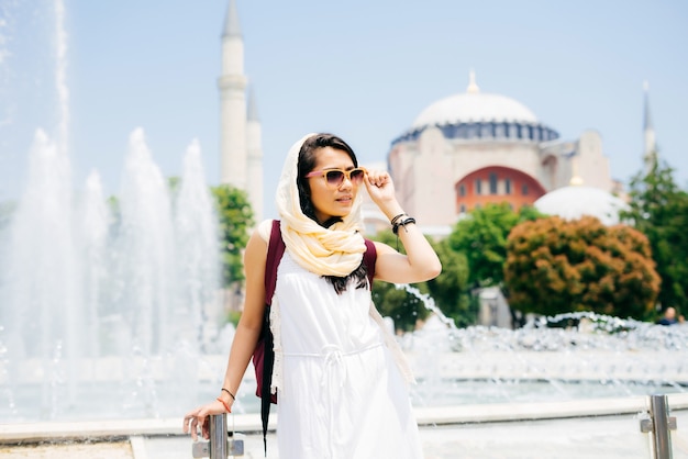 Fashion portrait of a young modern Muslim woman on summer holidays dresses glasses, looks afar, a mosque on the background. Summer trip, vacation