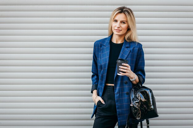 Fashion portrait of young stylish hipster woman walking on the street, wearing cute trendy outfit and drinking tasty coffee