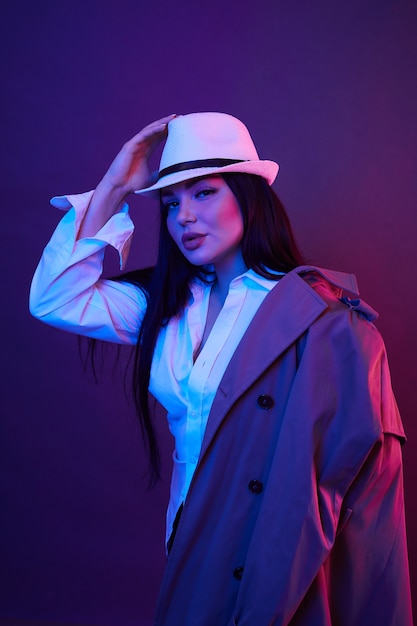 Fashion portrait of young woman in coat and hat in the studio with neon color filters