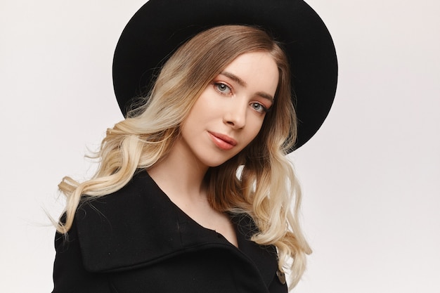 A fashion portrait of a young woman with gentle makeup and a black hat, isolated on white studio background