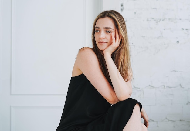 Fashion portrait of young woman with long hair on evening elegant black dress in white interior