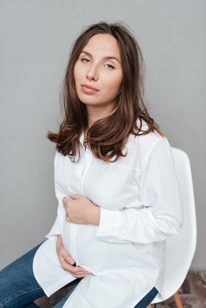 Fashion pregnant woman in studio ssitting on a chair isolated gray background