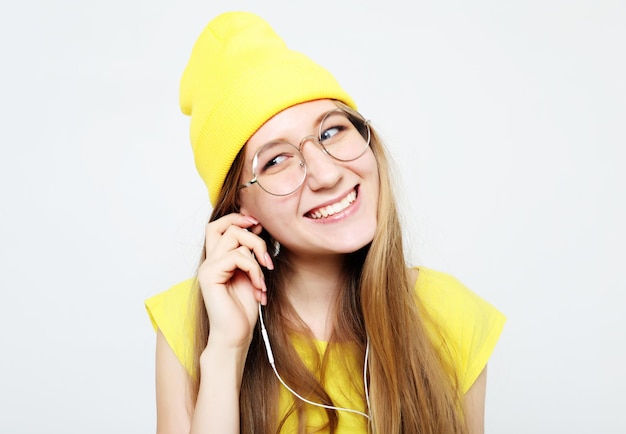 白い背景の上に黄色の帽子とTシャツを着て音楽を聴いているヘッドフォンでかなりクールな女の子をファッション