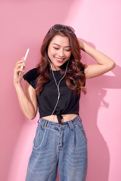 Fashion pretty cool smiling girl, relaxing, listening to music with headphones on a pink wall.