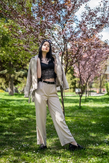 Fashion pretty girl posing near blooming tree branches in spring