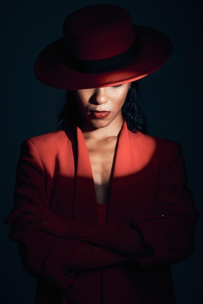 Модный красный костюм с прожектором для женщины в темной тайне и ретро 90-х на черном фоне студии Дизайнерская сила и модель со скрещенными руками в винтажной одежде и макияжем для расширения возможностей