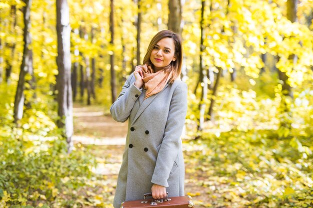 fashion, season and people concept - happy young woman is going on a trip with retro suitcase on a