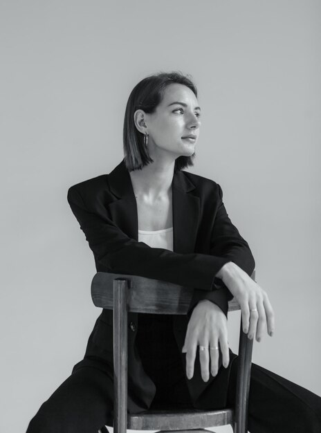 スタジオの椅子に座っている黒いスーツを着た若いスタイリッシュな女性のファッションショット